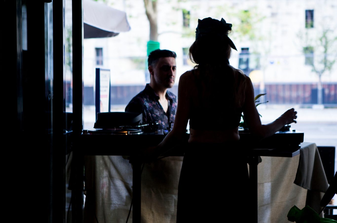 Silhouette d'une femme au bar, avec un homme en arrière-plan. Éclairage tamisé.