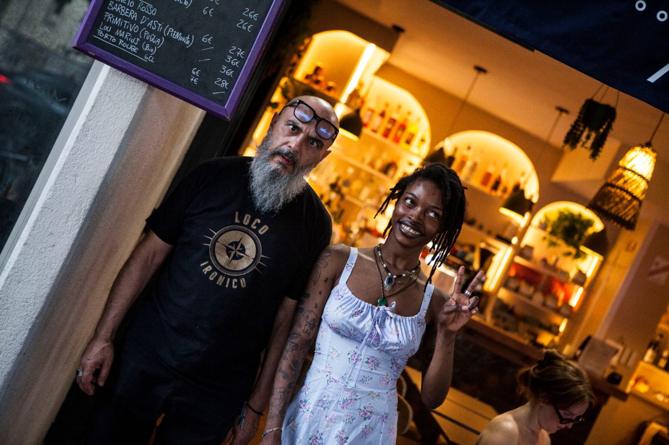 Deux personnes souriantes dans un café, l'une faisant signes de paix.