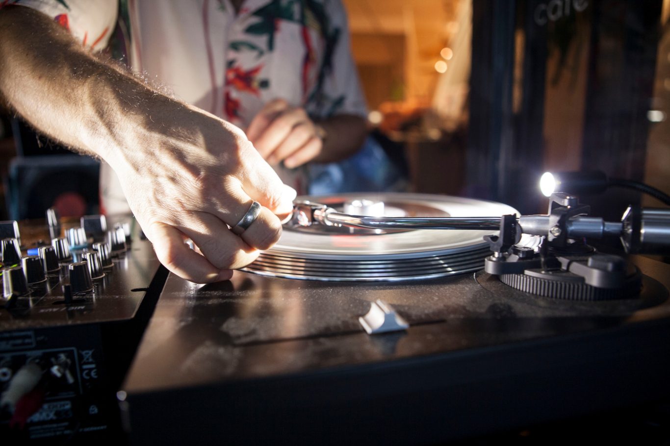 Une main ajuste un vinyle sur une platine de DJ dans un environnement tamisé.