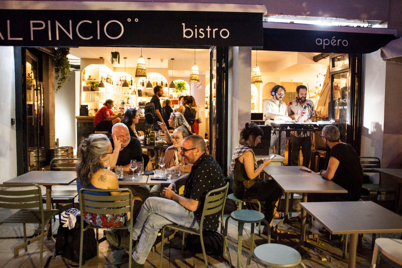 Groupe de personnes assises à des tables en extérieur d'un bistrot animé le soir.