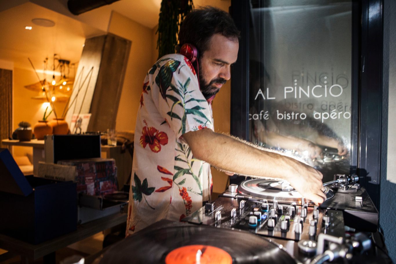Un DJ mixant des disques, portant une chemise à fleurs, dans un cadre moderne.