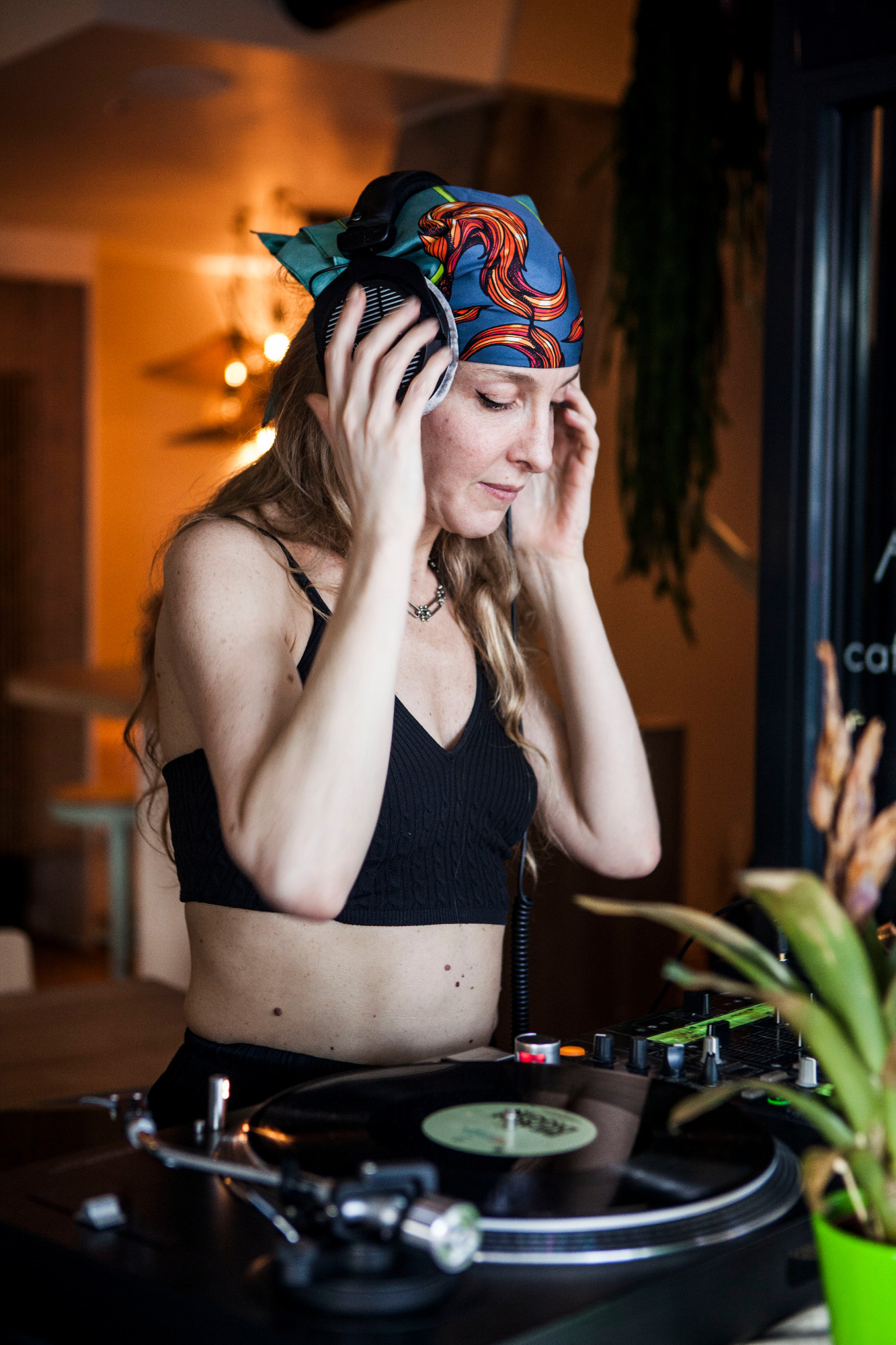 Femme DJ coiffée d'un bandana, mixant avec des platines dans un cadre intérieur.