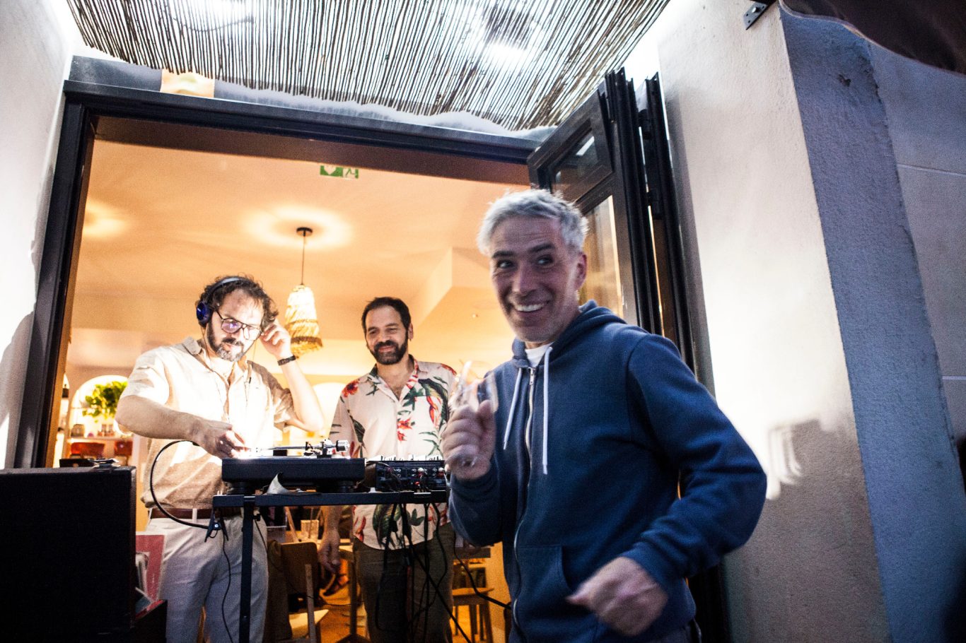 Un homme souriant pose devant deux musiciens à l'intérieur d'un café.