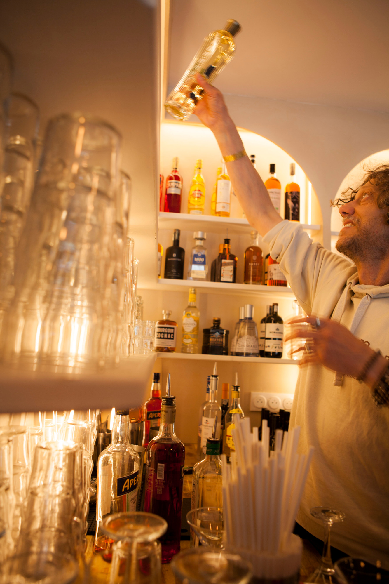 Un barman versant une bouteille dans un bar aux étagères éclairées.