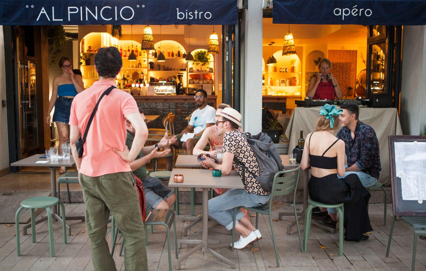 Des personnes assises à une table extérieure d'un bistro vivant, discutant en groupe.