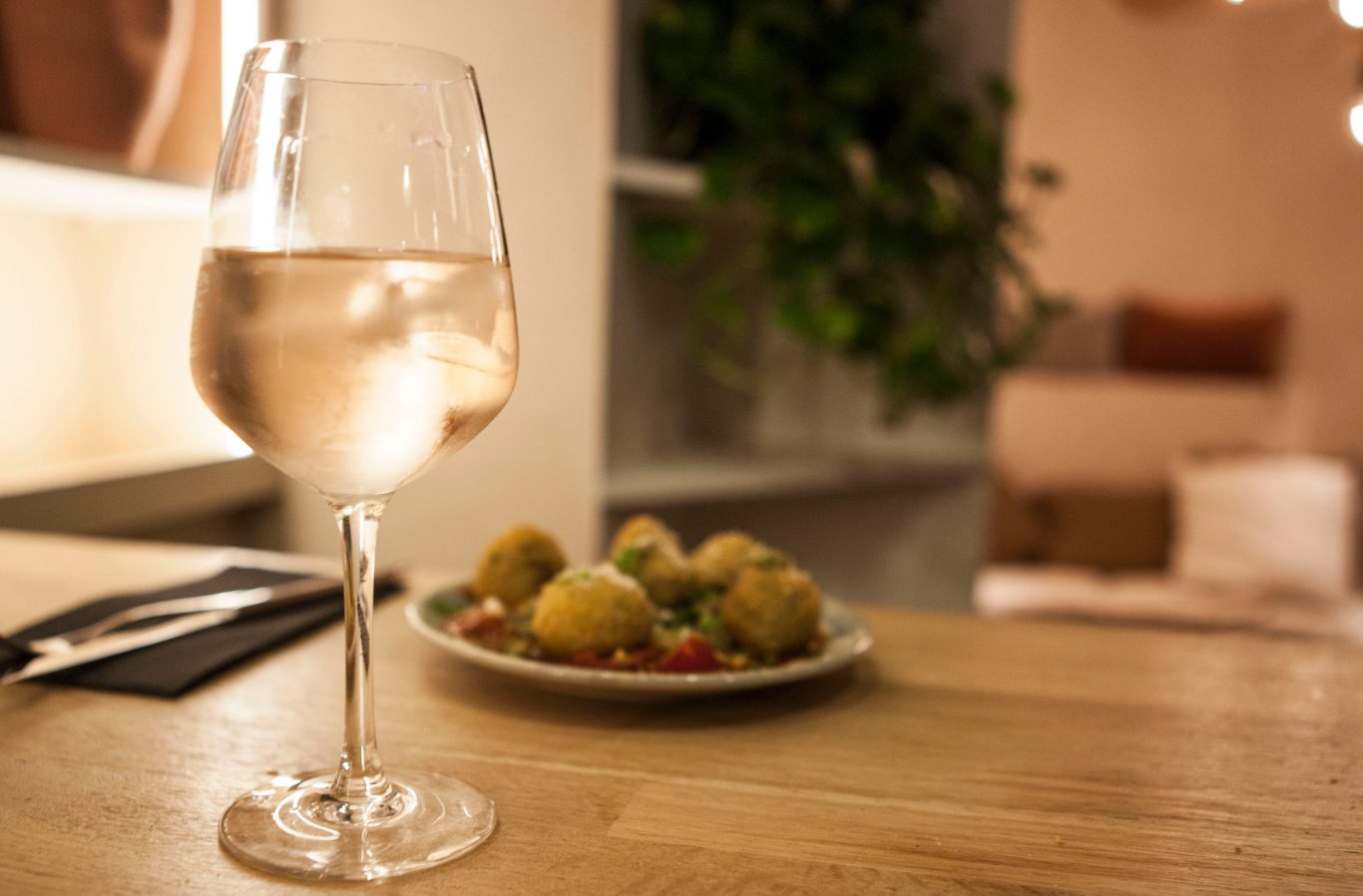 Un verre de vin rosé posé sur une table, avec une assiette d'olives en arrière-plan.