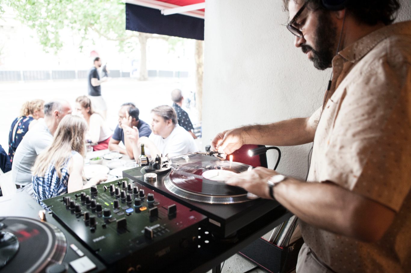 Un DJ joue des vinyles pendant un événement, des personnes écoutent autour de lui.